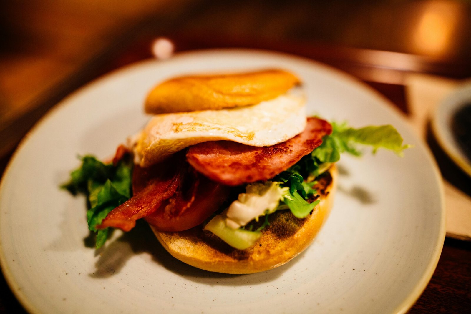 Tasty breakfast sandwich featuring egg, bacon, lettuce, and tomato on a bun.